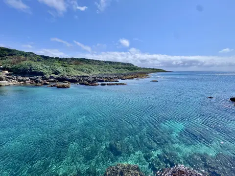 恆春半島清澈海岸 · turquoise 海水透到底、看得見海底礁石，遠岸線綠色植被與淡淡的雲